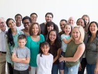 Große Gruppe von lachenden Erwachsenen und Kindern unterschiedlicher Herkunft steht eng zusammen vor weißem Hintergrund.