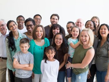 Copyright: Canva Große Gruppe von lachenden Erwachsenen und Kindern unterschiedlicher Herkunft steht eng zusammen vor weißem Hintergrund.