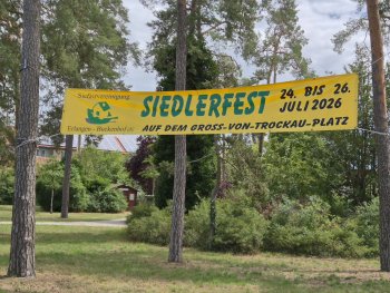 Ein Wald mit einem Hinweisbanner auf das Siedlerfest.