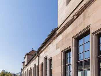 Historisches Sandsteingebäude mit großen Sprossenfenstern, an dem ein Banner mit der Aufschrift „Eingang“ zum Kulturzentrum hängt.