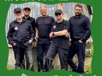 Ein Foto von fünf Personen in schwarzer Arbeitskleidung, die nebeneinander vor einer verwitterten Metallwand stehen. Oben links steht in weißer Schreibschrift „live am 22.Mai".
