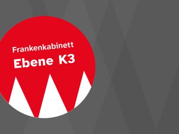Roter Kreis mit weißen Zacken und der Aufschrift „Frankenkabinett Ebene K3“ vor grauem Hintergrund.