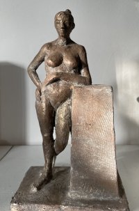 Bronzeskulptur einer stehenden weiblichen Aktfigur, die sich mit einem Arm auf einen quaderförmigen Sockel stützt.