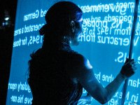 Eine Person steht als Silhouette vor einer blau beleuchteten Projektionswand mit Text und hält eine senkrechte Stange.