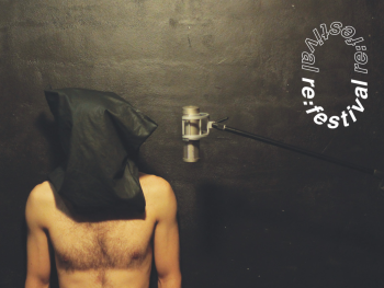Barfüßige Person mit dunklem Stoff über dem Kopf steht vor einer Wand mit Mikrofon, daneben das Logo „re:festival“.