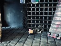 Miniaturmodell einer Gefängniszelle mit Gitterstäben, hinter denen ein Skelett liegt, während davor ein Kuchenstück auf dem Steinboden steht.