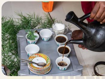 Eine Person schenkt Kaffee aus einer traditionellen schwarzen Tonkanne in kleine Tassen bei einer äthiopischen Kaffeezeremonie.