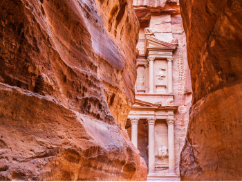 Blick durch die enge Felsschlucht Siq auf die in Sandstein gehauene Fassade des Schatzhauses Al-Khazneh in Petra.