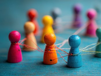 Copyright: AdobeStock Bunte Holzfiguren sind mit bunten Fäden netzwerkartig miteinander verbunden und stehen auf einer blauen Oberfläche