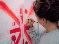 Frau schreibt mit Bleistift auf einen gelben Zettel an einer Wand mit roter abstrakter Bemalung