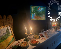 Festlich gedeckter Tisch mit Kerzenleuchtern, Fingerfood und Gläsern vor einem beleuchteten Bild mit religiöser Illustration, daneben ein Gemälde mit Zypressenlandschaft.