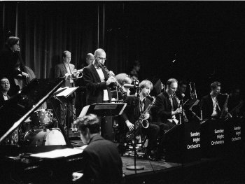 In schwarz-weiß ist eine große Band zu sehen mit vielen Instrumenten.