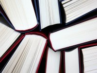 Mehrere Bücher mit dunklem Einband liegen im Kreis angeordnet, sodass ihre aufgeschlagenen Seiten in die Bildmitte zeigen.