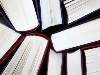 Mehrere Bücher mit dunklem Einband liegen kreisförmig angeordnet mit den aufgeschnittenen Seiten zur Mitte.
