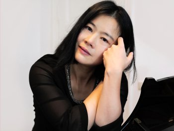 Copyright: Xiao Seibold Eine Frau in schwarzer Bluse stützt ihren Kopf auf die Hand und lehnt sich an einen Flügel.