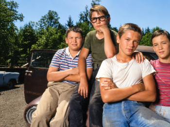 Copyright: Studiocanal
Vier Jungen mit verschränkten Armen posieren auf einem alten Auto auf einem Schrottplatz vor Bäumen.