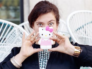 Copyright: Heike Bogenberger Eine Person hält sich eine Handyhülle in Form einer Hello-Kitty-Figur vor das Gesicht und blickt über den Rand hinweg in die Kamera.