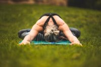 Eine Person übt auf einer Yogamatte im Gras eine Vorbeuge im Schmetterlingssitz.