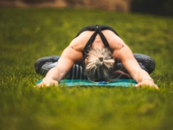 Eine Person übt auf einer Yogamatte im Gras eine Vorbeuge im Schmetterlingssitz.