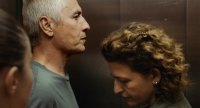 Zwei Personen stehen dicht beieinander, im Vordergrund eine Person mit lockigem Haar und im Profil eine Person mit weißen Haaren.