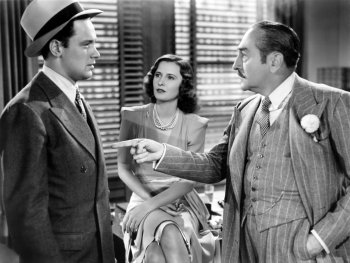 Copyright: Filmverleih Schwarz-Weiß-Filmszene, in der ein Mann im Nadelstreifenanzug auf einen jüngeren Mann mit Hut zeigt, während eine Frau im Hintergrund zusieht.