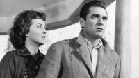 Schwarz-weißes Filmfoto einer Frau und eines Mannes, die mit besorgter Miene nach oben blicken.