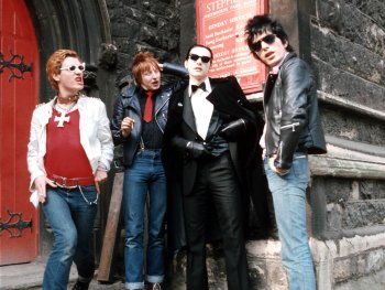Copyright: Filmverleih Vier Personen in Punk- und Rockabilly-Kleidung mit Sonnenbrillen und Lederjacken posieren vor dem Eingang einer Kirche.