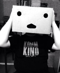 Person mit Kartonschachtel als Maske über dem Kopf und T-Shirt mit der Aufschrift „Komm Kind“ in schwarz-weißer Aufnahme.