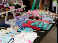 Bunte gefaltete Kinderkleidung mit Preisschildern liegt auf mehreren Tischen bei einem Flohmarkt oder Second-Hand-Verkauf.