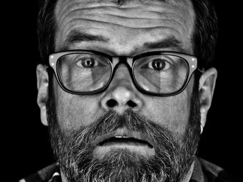 Copyright: Juergen Spachmann Schwarz-weißes Porträt einer bärtigen Person mit Brille und Karohemd, die mit ernstem Blick direkt in die Kamera schaut.