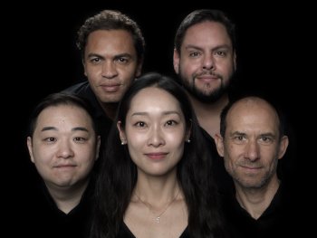 Harmonüx: Fünf Personen in dunkler Kleidung blicken dicht nebeneinander angeordnet vor schwarzem Hintergrund in die Kamera.