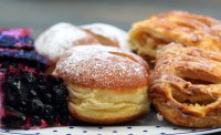 Nahaufnahme eines Tellers mit gepuderten Krapfen, Apfeltaschen und Blaubeerkuchenstücken.