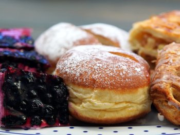 Foto: pixaby
Nahaufnahme eines Tellers mit gepuderten Krapfen, Apfeltaschen und Blaubeerkuchenstücken.