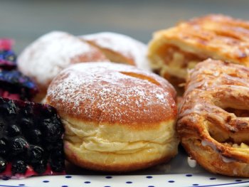 Nahaufnahme eines Tellers mit gepuderten Krapfen, Apfeltaschen und Blaubeerkuchenstücken.