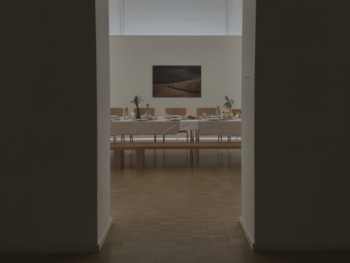 Blick durch einen Rundbogen in einen hellen Saal mit langer, festlich gedeckter Tafel und Blumenschmuck vor einer Wand mit gerahmtem Bild.