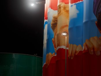 Große zylindrische Silos mit einem großflächigen Wandbild eines Kindes werden nachts von Scheinwerfern angestrahlt.