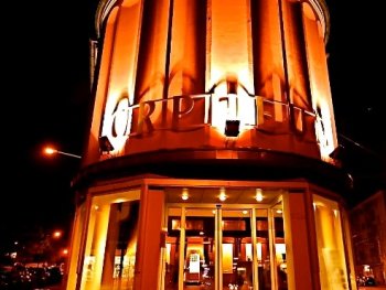 Nachts orange beleuchtete, runde Fassade des Kinos „Orpheum“ im Art-déco-Stil mit beleuchtetem Eingangsbereich.