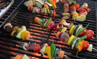 Mehrere bunte Gemüsespieße mit Paprika, Tomaten, Zwiebeln und Zucchini liegen auf einem glühenden Grillrost.