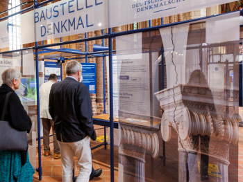 Copyright: Deutsche Stiftung Denkmalschut Blick in die Ausstellung Baustelle Denkmal: Besuchende betrachten Fotos von Säulen und die Beschreibung der Exponate.