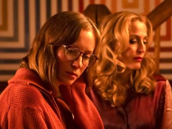 Copyright: MUBI Deutschland Zwei Frauen mit gesenktem Blick sitzen nebeneinander in warmem, rötlichem Licht vor einem gemusterten Hintergrund.