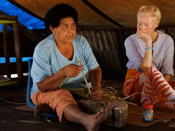 Copyright: filmgalerie451
Zwei Frauen sitzen auf dem Boden einer Hütte, während eine von ihnen Palmblätter zu einer Matte flicht.