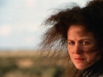 Copyright: NSFA
Nahaufnahme einer Person mit vom Wind zerzaustem lockigem Haar, die mit ernstem Blick in die Kamera schaut, im Hintergrund eine verschwommene Landschaft.