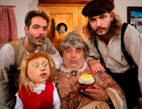 Drei Schauspieler in historischen Kostümen posieren mit einer Handpuppe und einer Schale Speiseeis vor einem Holzschrank mit kleiner Wichtelfigur.