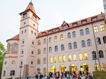 Menschen versammeln sich abends vor dem historischen Gebäude der Hochschule für Musik Nürnberg mit Uhrturm.