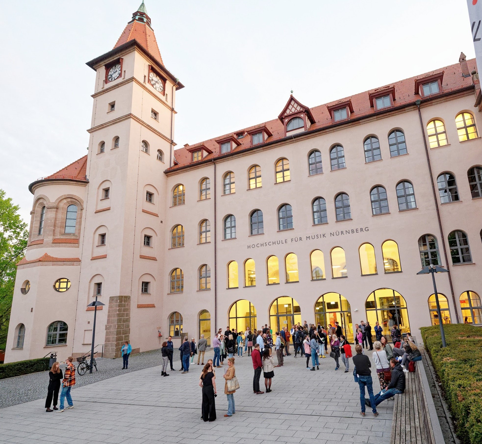 Menschen versammeln sich abends vor dem historischen Gebäude der Hochschule für Musik Nürnberg mit Uhrturm.