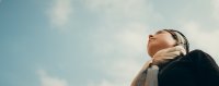 Person mit Kopftuch blickt vor blauem Himmel mit Wolken nach oben.