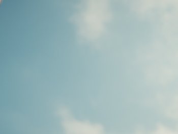Person mit Kopftuch blickt vor blauem Himmel mit Wolken nach oben.