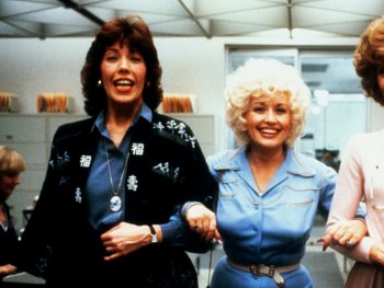 Copyright: Twentieth Century Fox
Drei lachende Frauen mit toupierten Frisuren gehen Arm in Arm durch ein Büro.