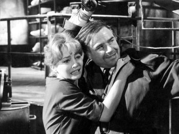 Copyright: Filmverleih
Schwarz-Weiß-Filmszene, in der ein Mann mit gefesselten Handgelenken eine ängstlich wirkende Frau in einer Industrieanlage schützend festhält.