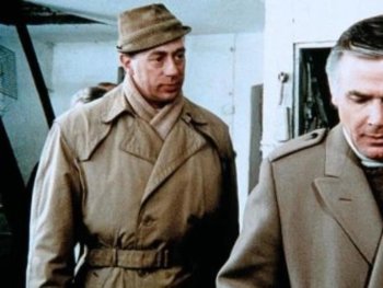 Copyright: Filmverleih
Zwei Männer in Mänteln stehen nebeneinander in einem Raum, einer mit Hut, beide mit nachdenklichem Ausdruck.